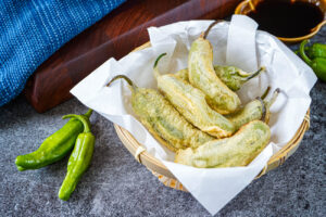 Shishito Tempura (Japanese Fried Shishito Peppers) in a bamboo basket lined with white paper.