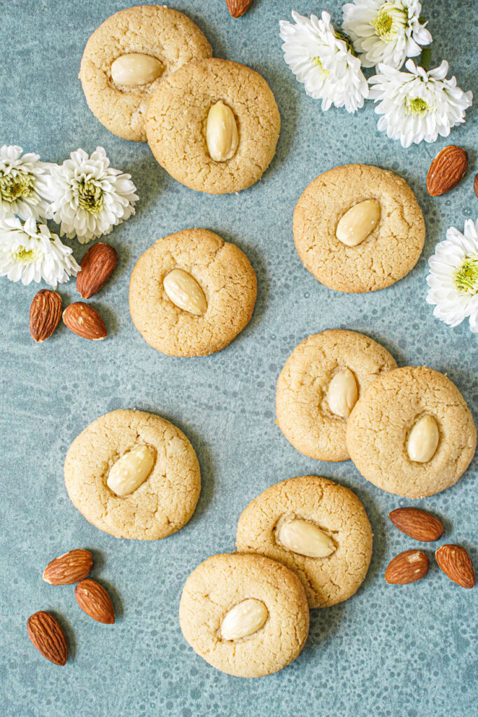 Aerial view of nine Tahina Cookies next to almonds and white flowers.