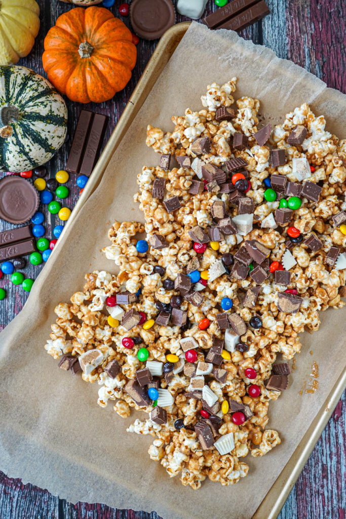 Aerial view of Halloween Candy Popcorn on a baking sheet next to candy and pumpkins.