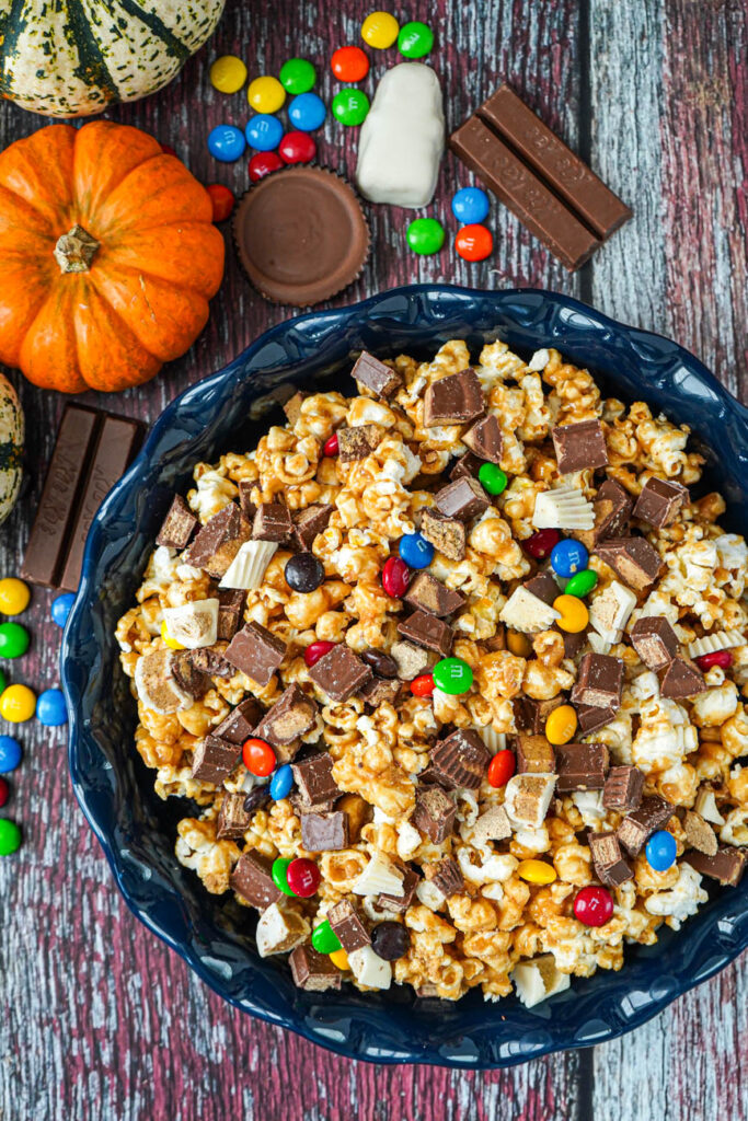 Aerial view of Halloween Candy Popcorn in a blue dish next to candy and pumpkins.