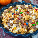 Halloween Candy Popcorn in a blue dish next to mini pumpkins and candy pieces.