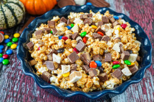 Halloween Candy Popcorn in a blue dish next to mini pumpkins and candy pieces.