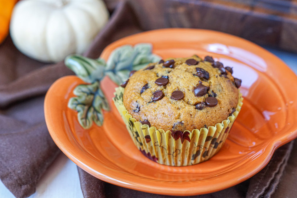 A Pumpkin Chocolate Chip Muffin on a pumpkin plate with a white pumpkin in the background.