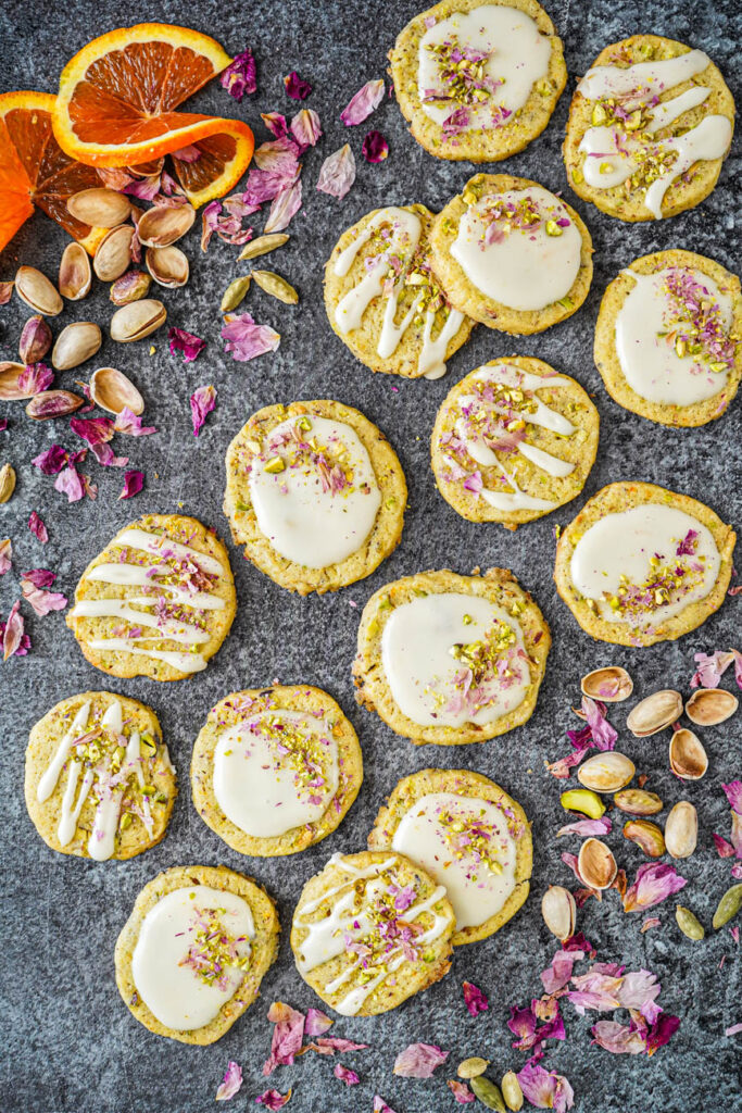 Aerial view of Orange Cardamom Cookies next to rose petals, orange slices, cardamom, and pistachios.