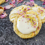 Three Orange Cardamom Cookies surrounded by pistachios, cardamom, and rose petals.