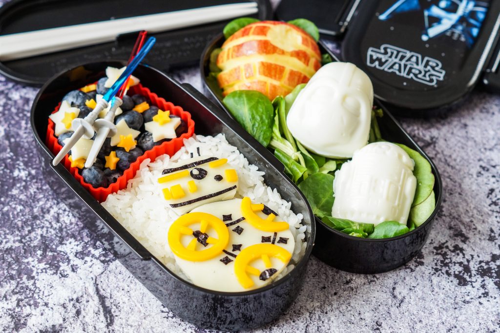 Star Wars Bento box filled with rice, cheese-shaped BB-8, eggs, Death Star-shaped apple, and blueberries.