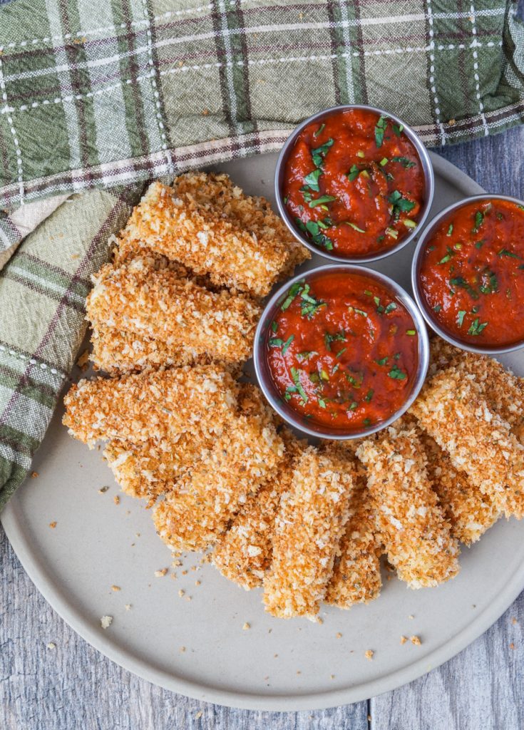Aerial view of Baked Mozzarella Sticks on a plate with three dipping bowls filled with marinara sauce.