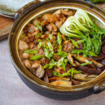 Clay Pot Chicken Rice with chicken, sausage slices, and bok choy over a layer of rice.
