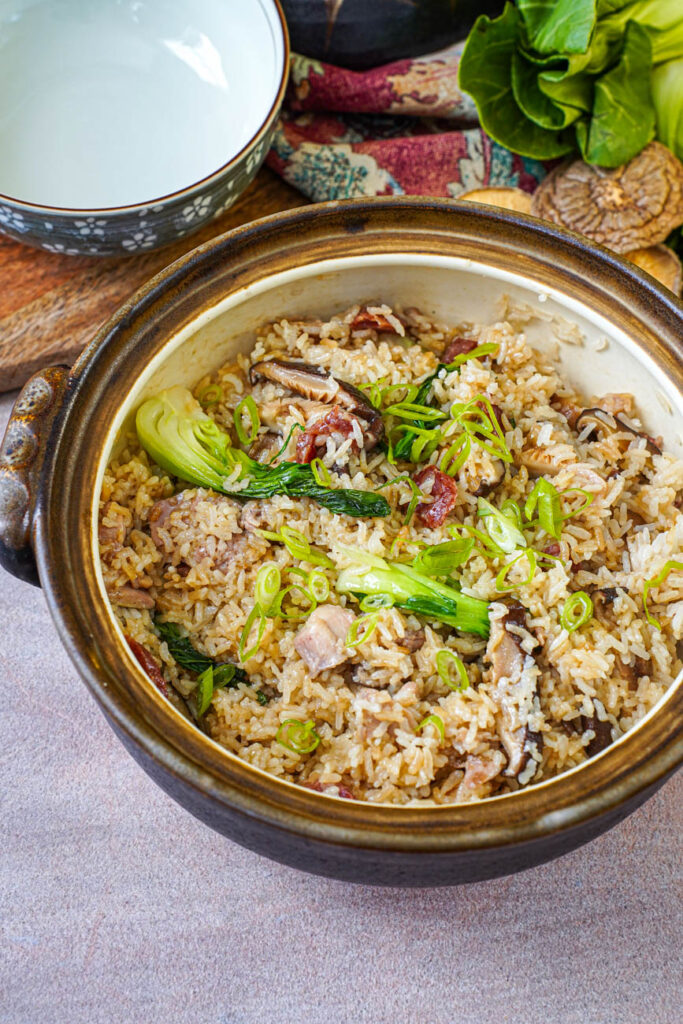Clay Pot Chicken Rice in a brown pot with the rice mixed with the bok choy, mushroom, chicken, and sausage.