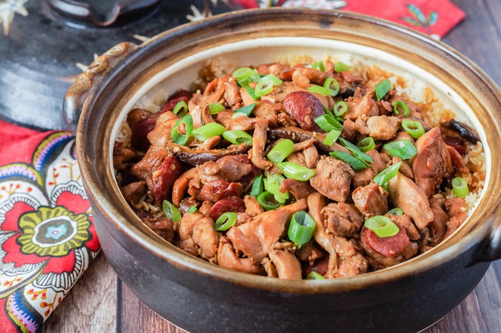 Claypot Chicken Rice in a large brown clay pot and topped with sliced green onions.