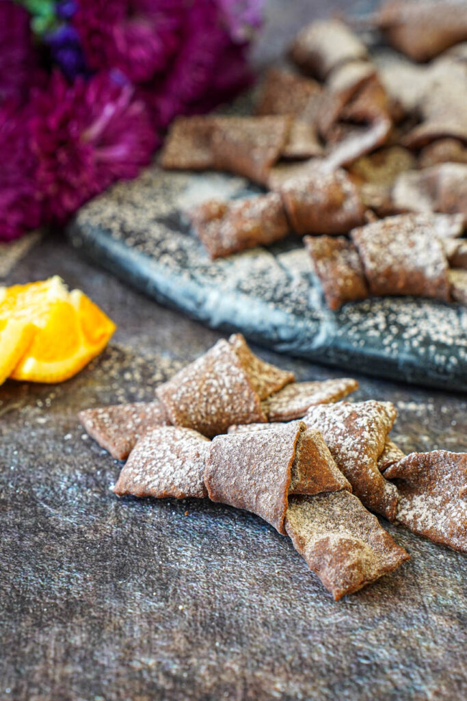 Three Crostoli al Cioccolato (Chocolate Crostoli) with more in the background on a marble board.