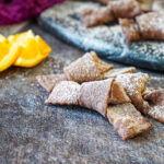 Crostoli al Cioccolato (Chocolate Crostoli) dusted in cocoa powdered sugar and next to orange wedges.