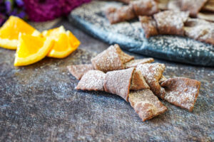 Crostoli al Cioccolato (Chocolate Crostoli) dusted in cocoa powdered sugar and next to orange wedges.