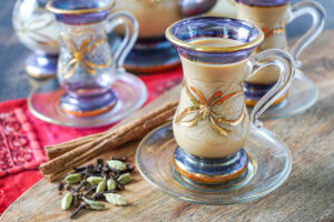 Shai Adeni (Adeni Tea) in two cups next to cardamom, cloves, and cinnamon.