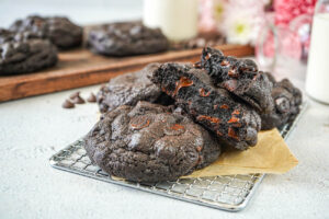 A pile of Dark Chocolate Cookies on a wire rack and piece of parchment.