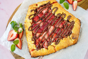 Strawberry Chocolate Hazelnut Galette on a piece of parchment next to strawberries and mint leaves.