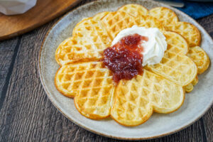 Two Äggvåfflor (Swedish Egg Waffles) on a plate with jam and whipped cream.