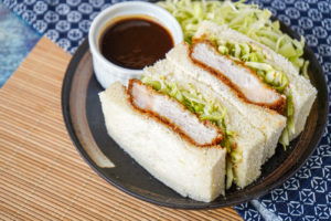 Two slices of Katsu Sando (Japanese Pork Cutlet Sandwich) on a dark brown plate with cabbage.