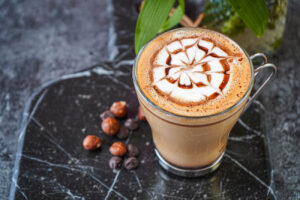 Chocolate Hazelnut Latte in a glass next to hazelnuts and chocolate chips.