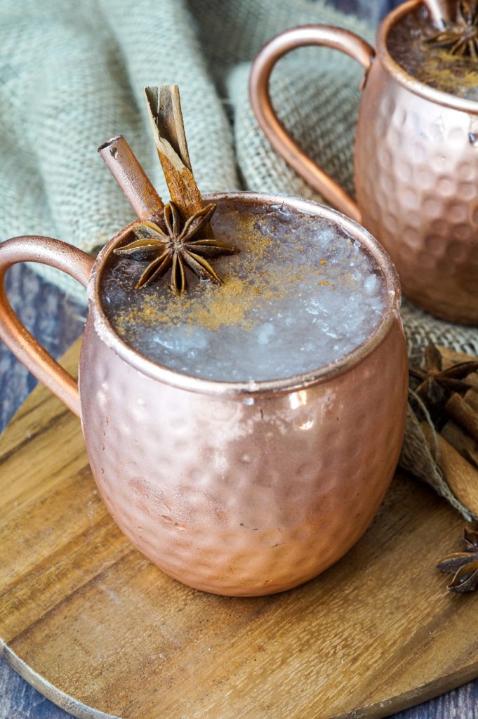 El Fusilado cocktail in two copper mule glasses on a wooden board.