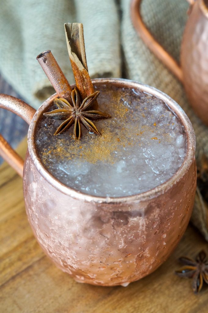 Close up of El Fusilado cocktail in a copper mule glass with two cinnamon sticks and star anise.
