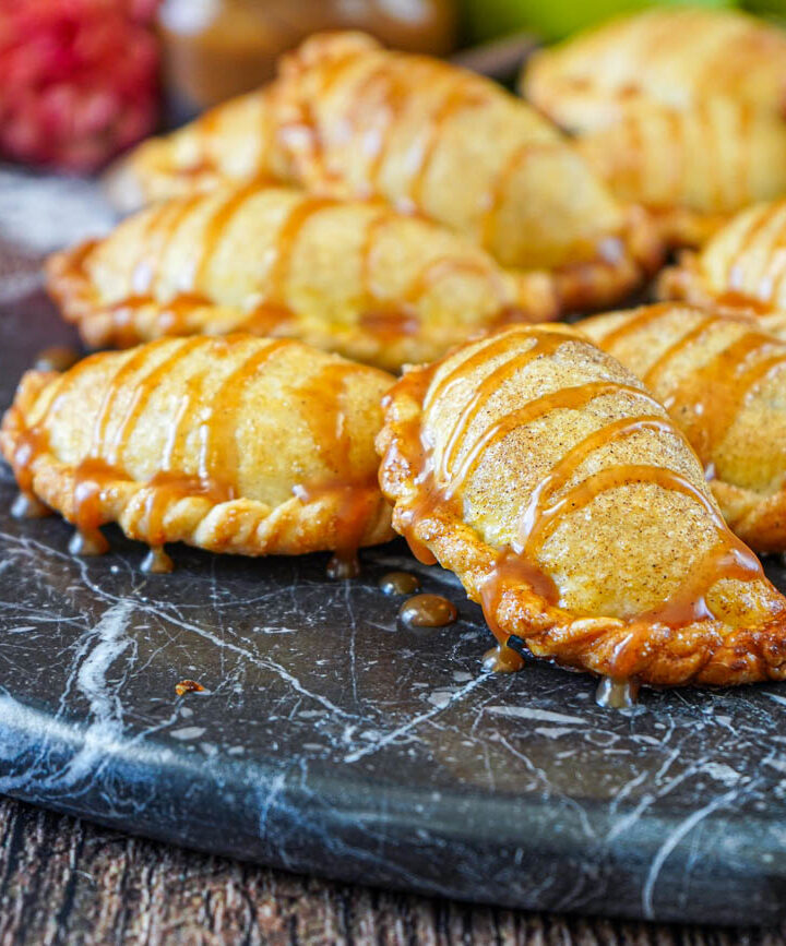 Caramel Apple Empanadas drizzled with caramel sauce on a wooden board.
