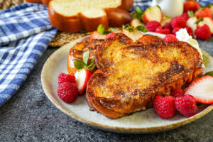Two slices Crème Brûlée French Toast on a plate with raspberries, strawberries, and whipped cream.