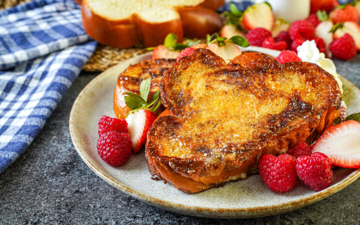 Two slices Crème Brûlée French Toast on a plate with raspberries, strawberries, and whipped cream.