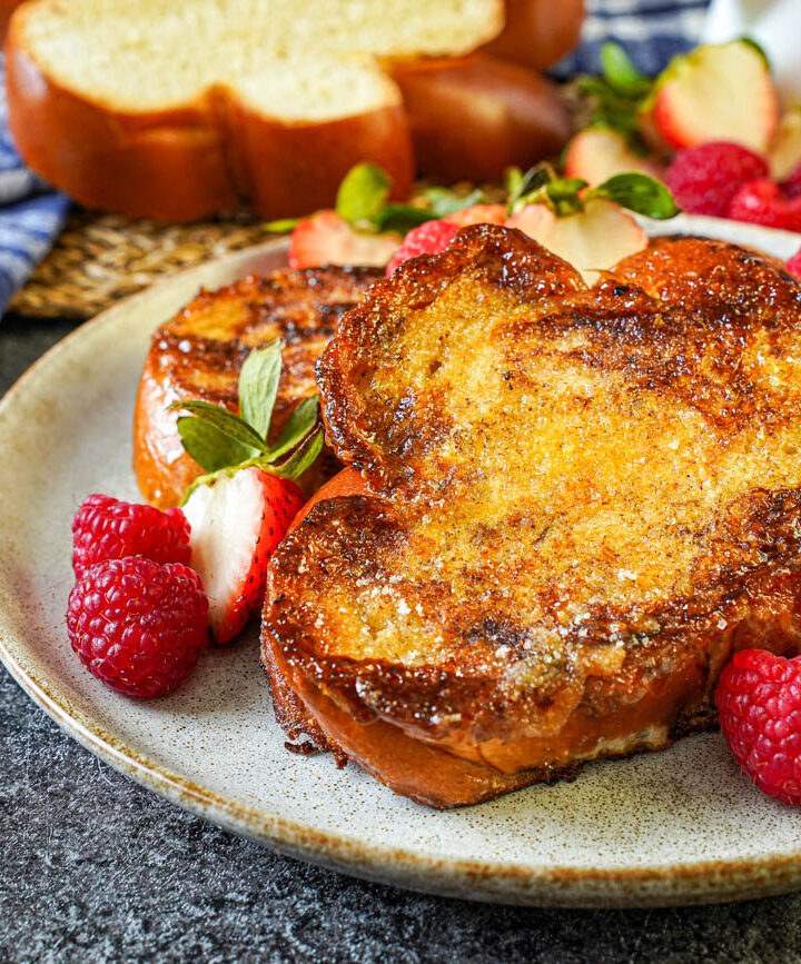 Two slices Crème Brûlée French Toast on a plate with raspberries, strawberries, and whipped cream.