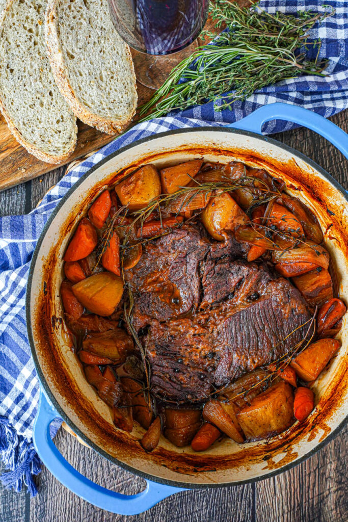 Aerial view of Beef Chuck Roast in a Dutch oven with potatoes, carrots, rosemary, and thyme.