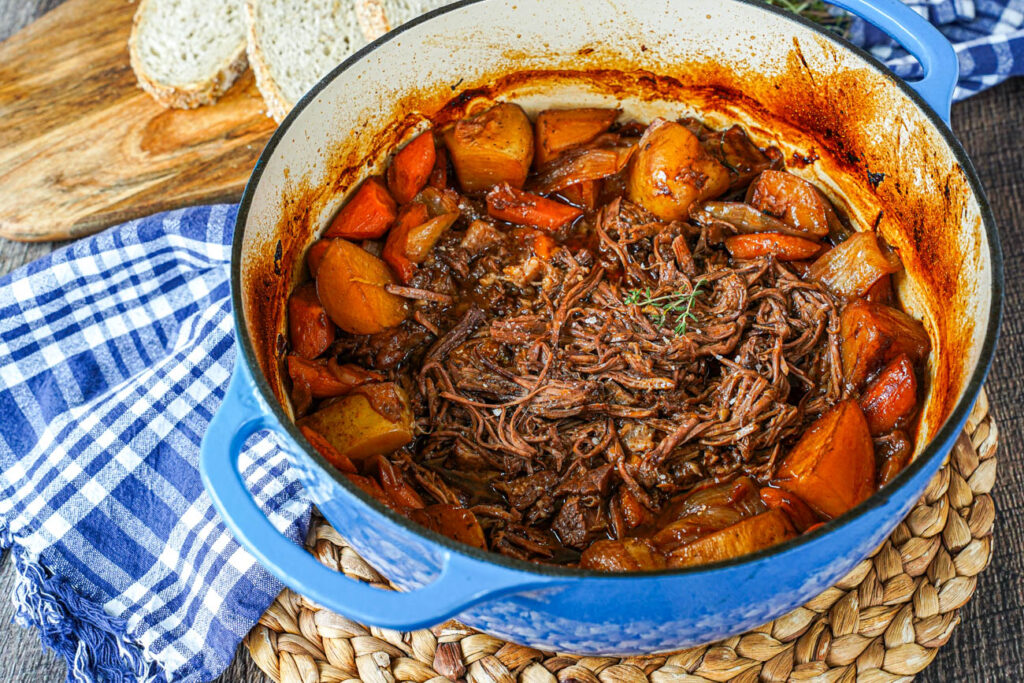 Beef Chuck Roast shredded in a blue dutch oven with potatoes and carrots.