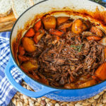 Beef Chuck Roast shredded in a blue Dutch oven with carrots and potatoes.