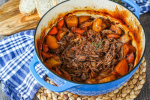 Beef Chuck Roast shredded in a blue Dutch oven with carrots and potatoes.