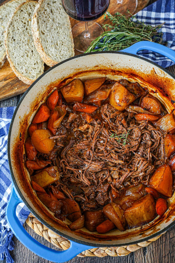 Aerial view of shredded Beef Chuck Roast in a Dutch oven with potatoes and carrots.