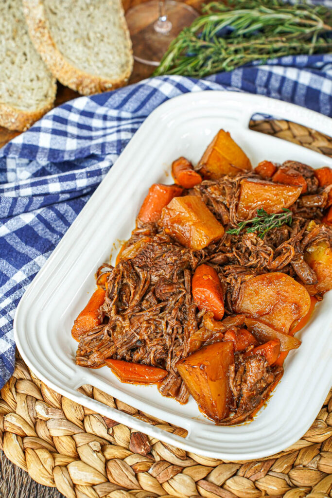 Shredded Beef Chuck Roast on a white platter with potatoes and carrots.