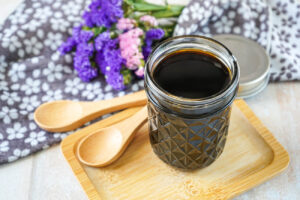 Homemade Teriyaki Sauce in a glass jar on a wooden board next to two wooden spoons and purple flowers.