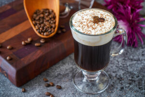 Irish Coffee in a glass topped with grated chocolate and three coffee beans.