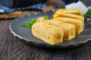 Dashimaki Tamago (Japanese Omelette Rolls) on a gray plate next to a shiso leaf and grated daikon.