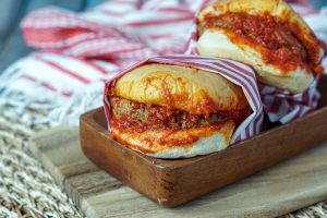 Two Islak Burger on a wooden board and wrapped in red/white paper.