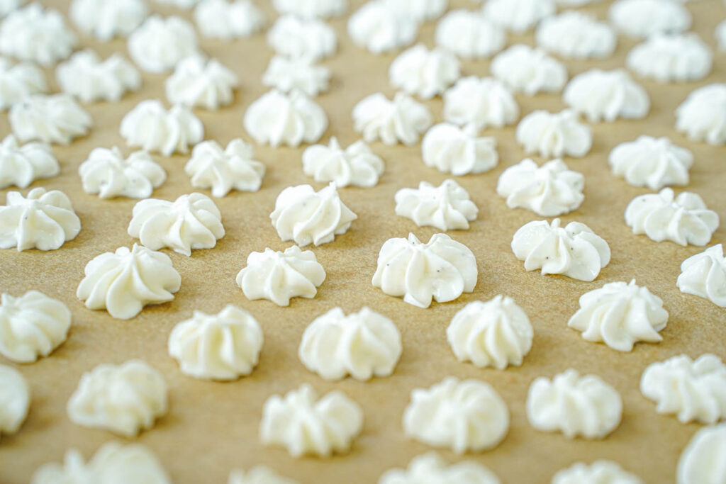 Side view of Vanilla Bean Frozen Yogurt Drops piped onto a tan piece of parchment.