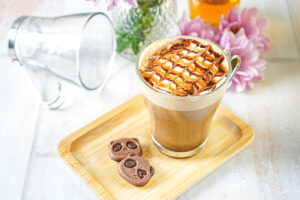Caramel Mocha Latte in a glass on a wooden tray next to two panda cookies.