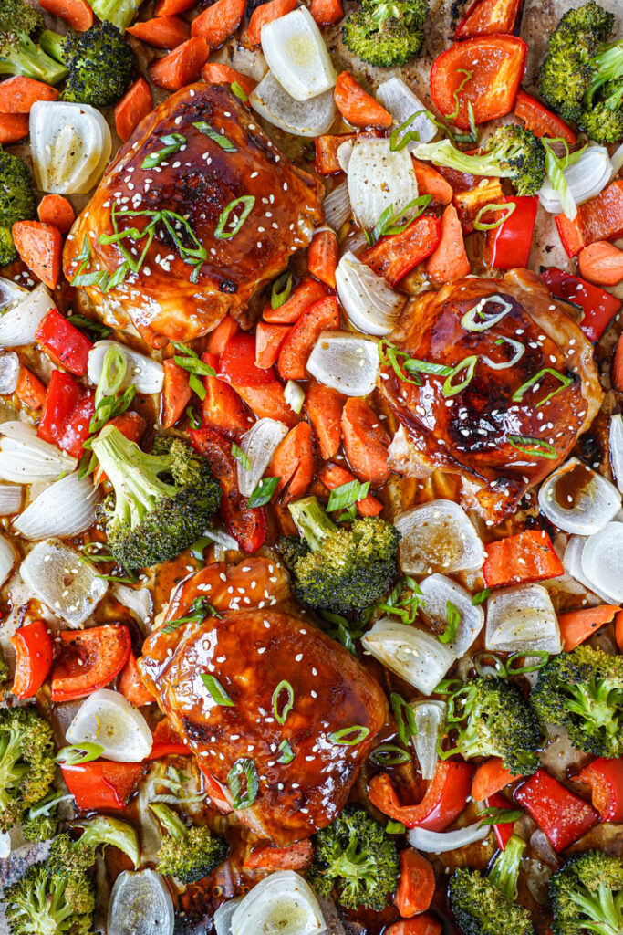 Aerial view of three Baked Teriyaki Chicken thighs on a baking sheet with roasted vegetables.