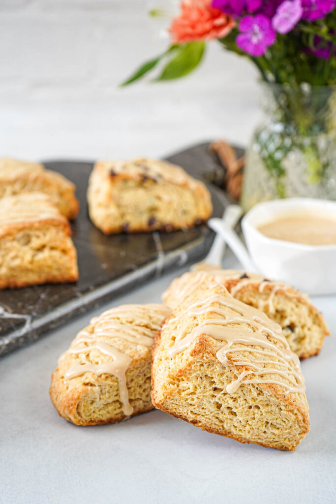 Side view of Irish Cream Scones with a bowl of Irish cream glaze and a vase with fresh flowers in the background.