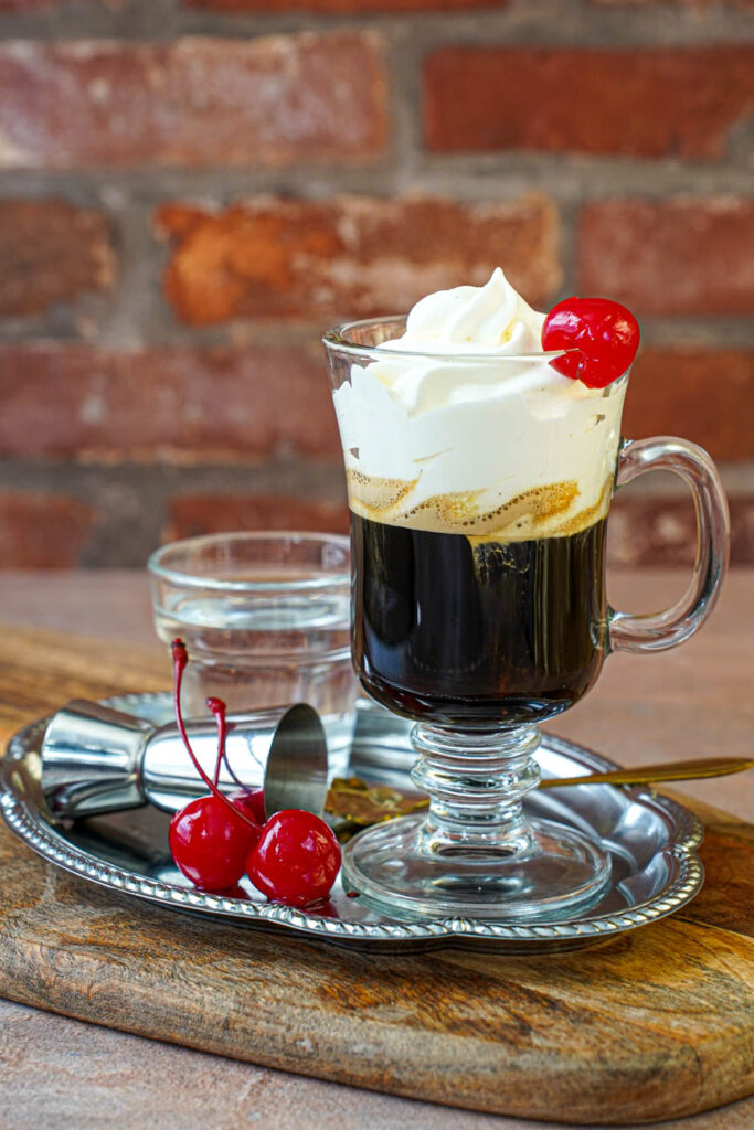 Side view of Einspänner (Viennese Coffee with Whipped Cream) with a cherry on the glass and two cherries on the tray.