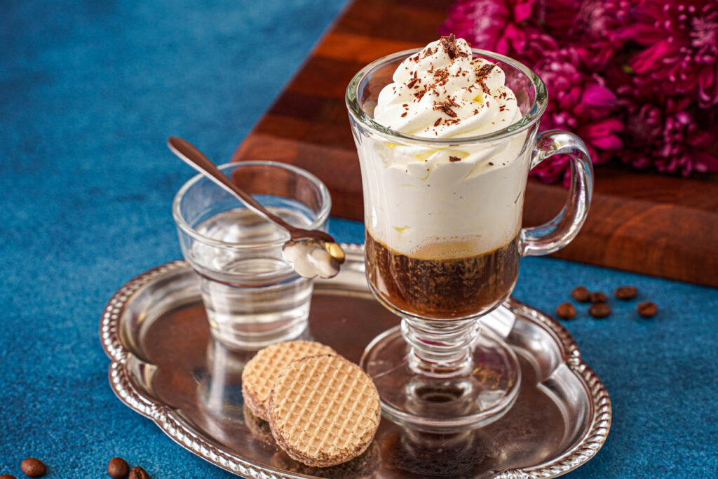 Einspänner (Viennese Coffee with Whipped Cream) on a tray with two cookies and a cup of water.