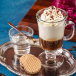 Einspänner (Viennese Coffee with Whipped Cream) on a tray with two cookies and a glass of water.