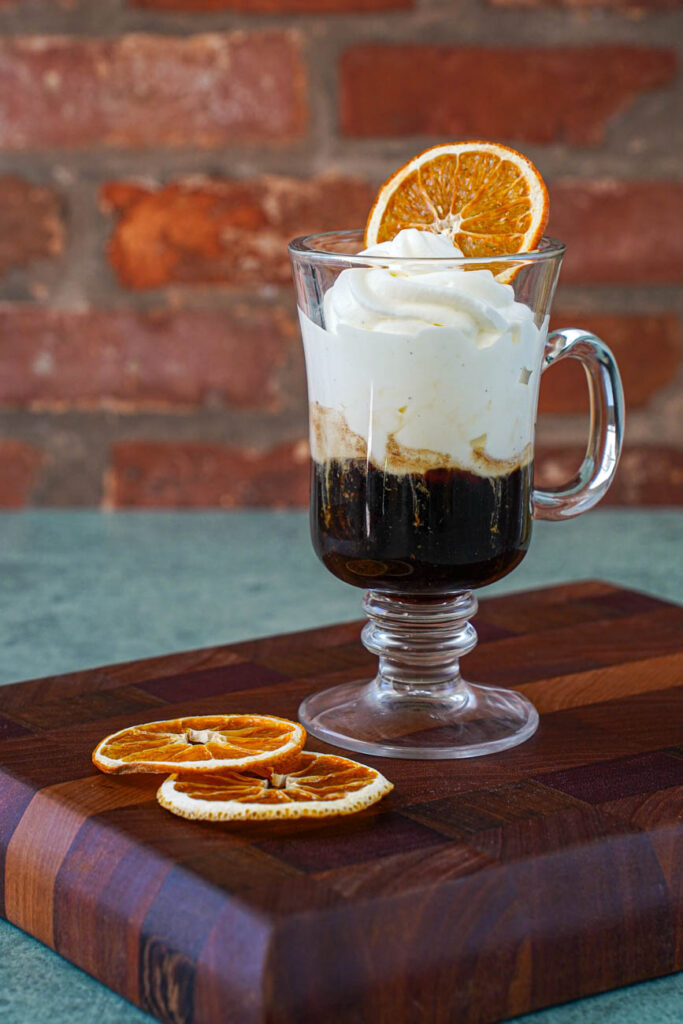 Einspänner (Viennese Coffee with Whipped Cream) in a glass with an orange slice on top.