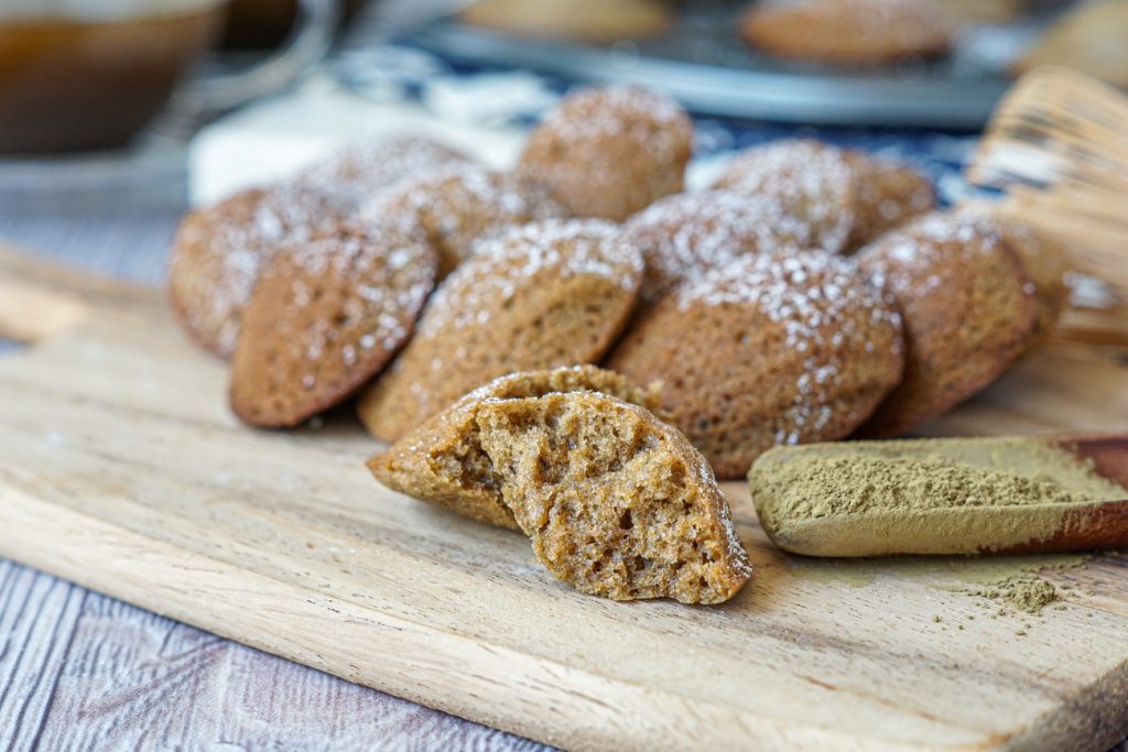 Hojicha Madeleines Hojicha Madeleines on a wooden board next to a scoop of hojicha powder.