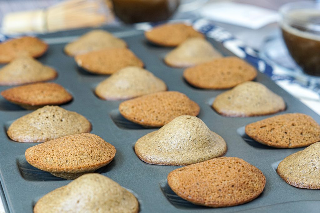 Hojicha Madeleines Madeleines in a Madeleine pan with tea in the background.