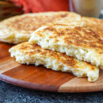 Mkatra Foutra (Sesame Coconut Flatbreads) on a wooden board with one torn in half to show fluffy texture.
